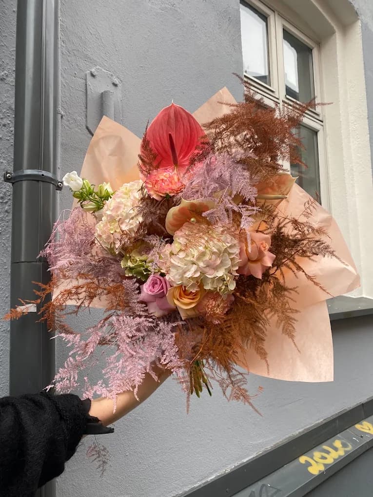 A large bouquet of cream hydrangea, roses and dusty pink astilbe wrapped in peach paper