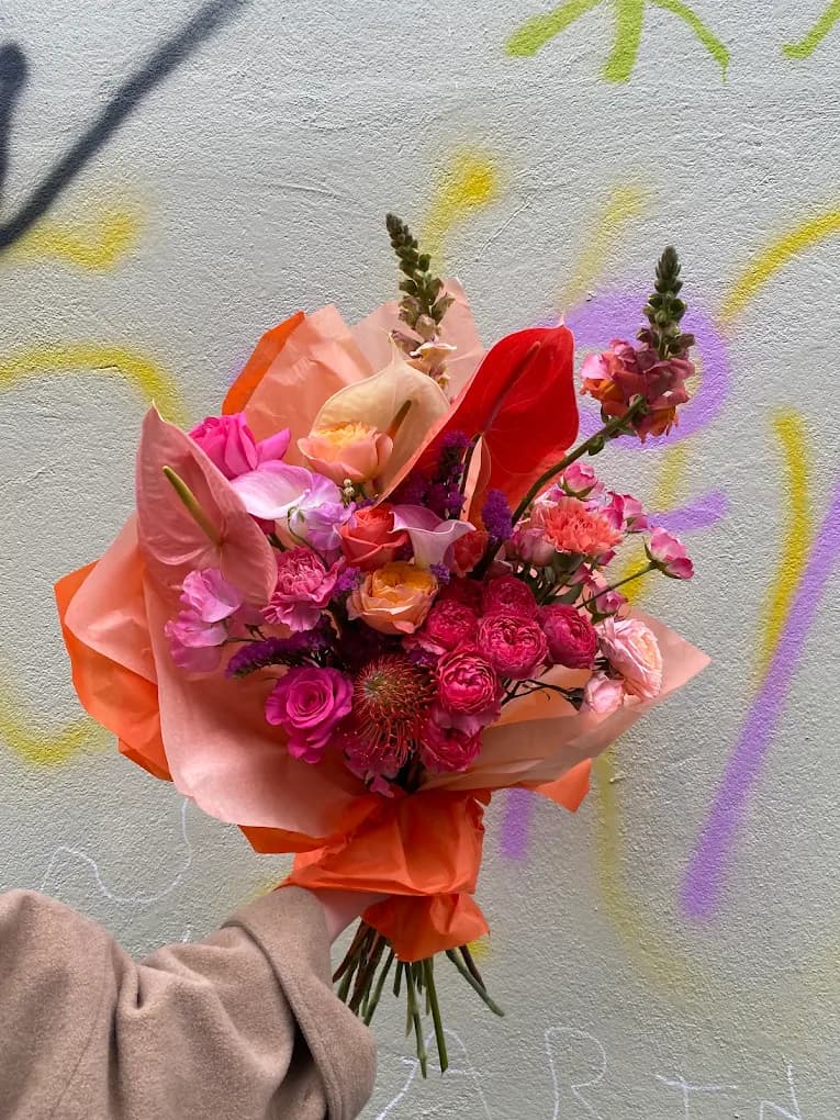 A big coral and pink bouquet with anthurium, roses and snapdragons wrapped in orange tissue